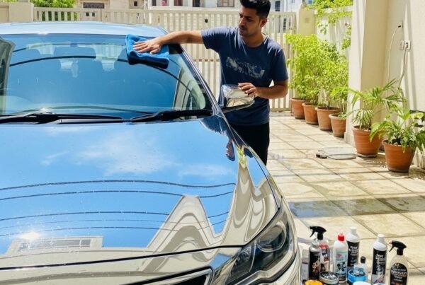 Man buffing a freshly washed car with a microfiber towel in a Karachi driveway, showing glossy paint, car shampoo, polish, and wax products nearby, highlighting professional car care and shine after wash.