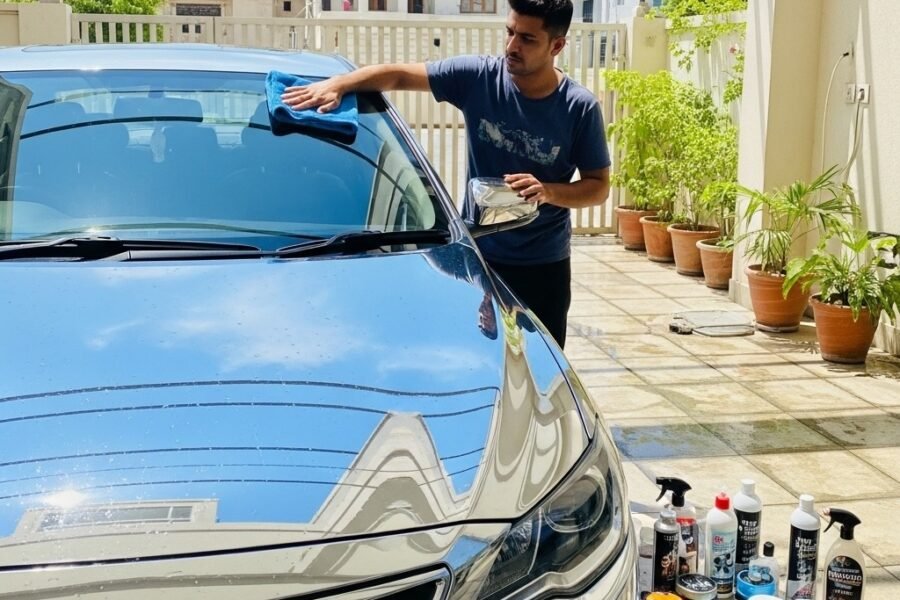 Man buffing a freshly washed car with a microfiber towel in a Karachi driveway, showing glossy paint, car shampoo, polish, and wax products nearby, highlighting professional car care and shine after wash.
