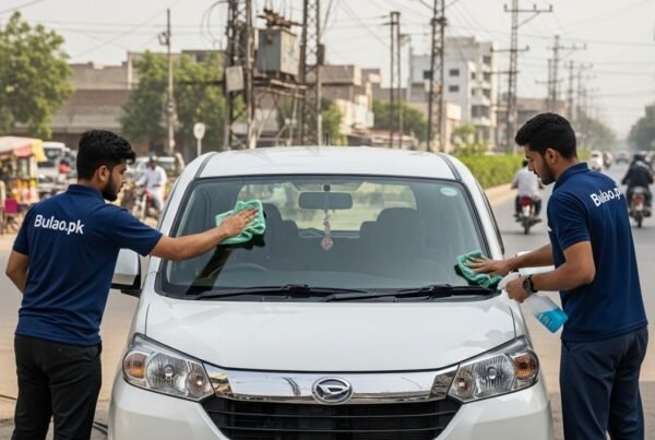 Two professional car cleaning technicians in navy blue Bulao.pk uniforms cleaning a shiny white Daihatsu Boon on a Karachi street, with a lively urban background and bright daylight, emphasizing a fresh and polished look.