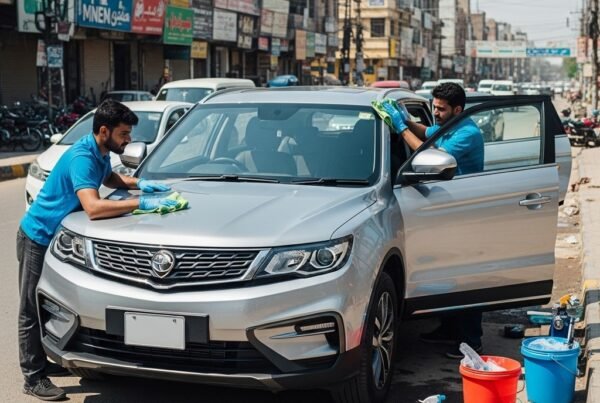 Two technicians detailing a silver Proton X70 SUV on a Karachi street. One wipes the hood with a microfiber cloth while the other cleans the dashboard through the open door. The SUV looks polished and shiny with no number plate visible, and Karachi’s shops and light traffic form the background.