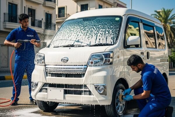 Professional car detailers cleaning a white Daihatsu Hijet compact van with foam wash and microfiber cloths, showcasing exterior detailing and wheel cleaning in a bright, realistic setting.